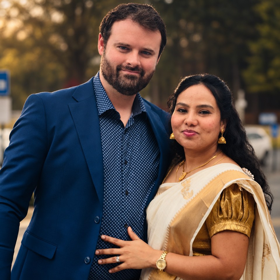 Dustin Whatley in a navy suit and Percy Whatley in a white and gold sari, standing together outdoors