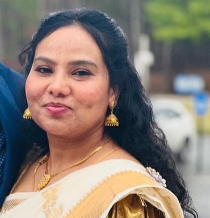 Percy Whatley in a white and gold sari with gold earrings and necklace, smiling outdoors