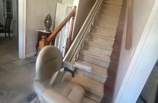Bruno curved stairlift at the foot of carpeted stairs, rail rising along the wall