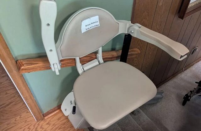 Bruno stairlift chair with arms raised at the top of carpeted stairs by wood panelling