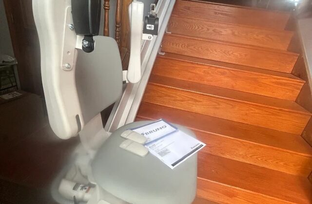Bruno stairlift folded at the foot of wooden stairs, owner manual resting on the seat