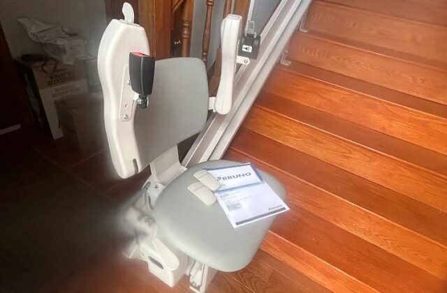 Bruno stairlift at the bottom of a wooden staircase beside a patterned rug