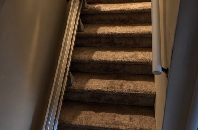 Bruno stairlift rail running up carpeted stairs with the chair parked at the top