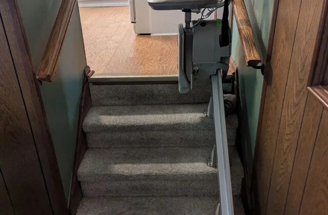 Bruno stairlift rail down carpeted stairs from a kitchen doorway, chair at the top