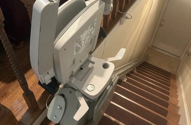 Bruno stairlift folded at the top of carpeted stairs beside a wooden banister