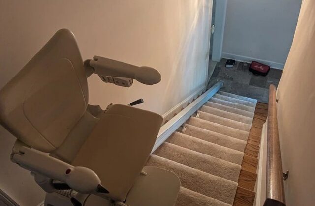 Handicare 1100 stairlift at the top of carpeted stairs leading down to a hallway