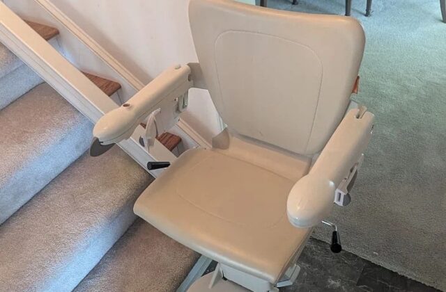 Handicare 1100 stairlift with arms down at the foot of stairs by a dining room