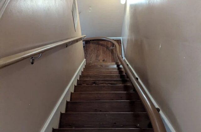 Handicare curved stairlift rail in brown curving down a narrow wooden staircase