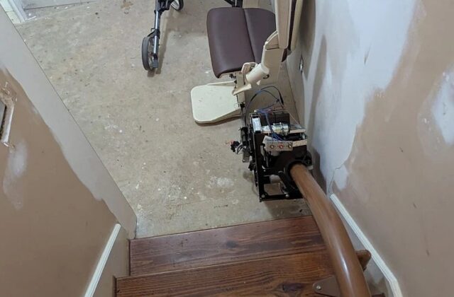 Handicare curved stairlift at the top of wooden stairs, a rollator on the landing