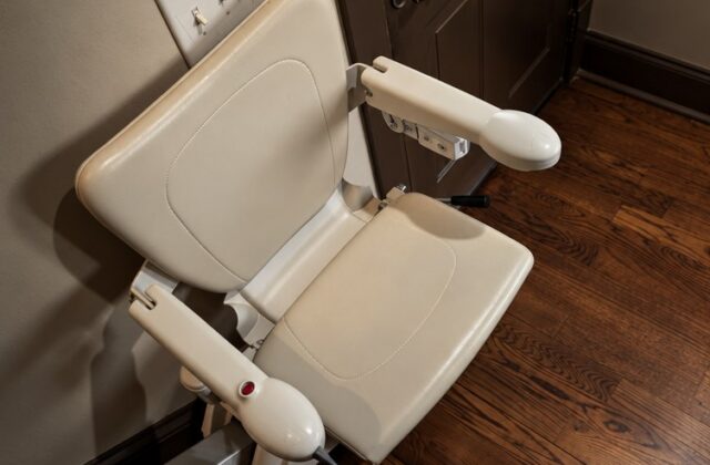 Handicare stairlift chair with arms folded down beside a back door, on a wooden floor