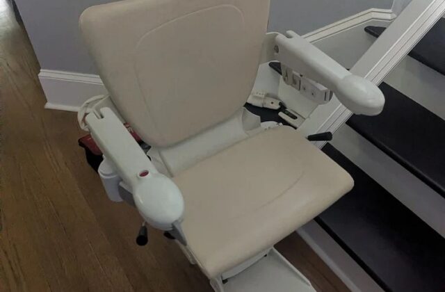 Handicare stairlift chair at the top of dark wooden stairs with the arms raised