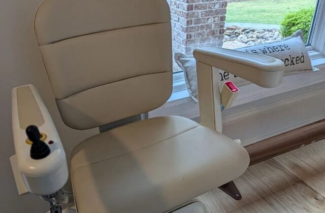 Handicare stairlift chair with a beige seat beside a window overlooking a garden