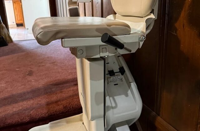 Handicare stairlift chair with footrest down at the foot of stairs by wood panelling