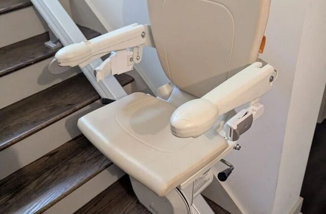 Handicare stairlift with arms down at the foot of dark wooden stairs