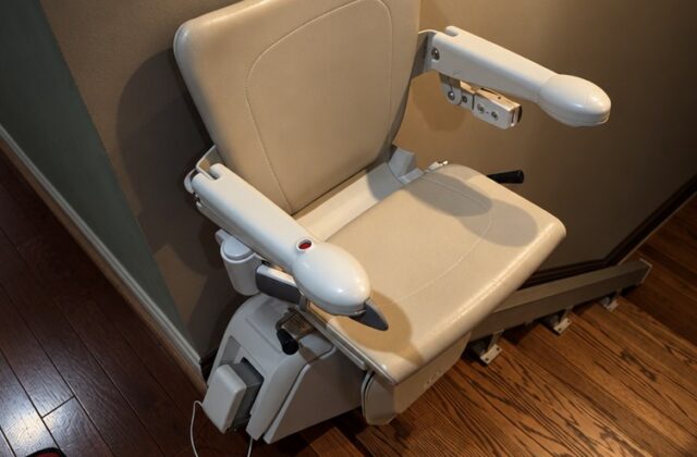 Handicare straight stairlift at the foot of wooden stairs with the seat and footrest folded down
