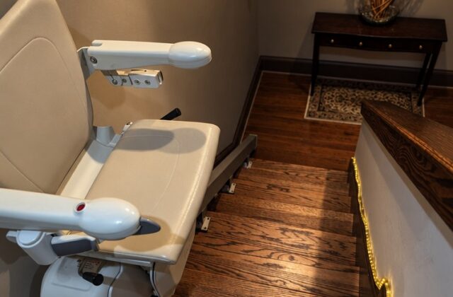 Handicare straight stairlift parked at the bottom of a wooden staircase beside a small hall table