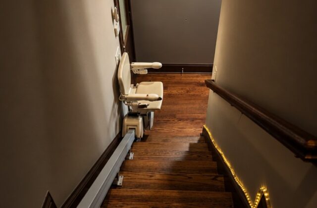 Handicare stairlift rail along a wooden staircase, seen from the top landing with the chair at the bottom
