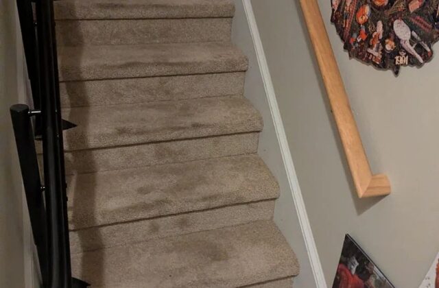 Handicare stairlift rail fitted along carpeted stairs opposite a wooden handrail
