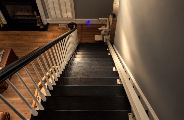 Handicare stairlift rail down dark wooden stairs into a living room with a fireplace