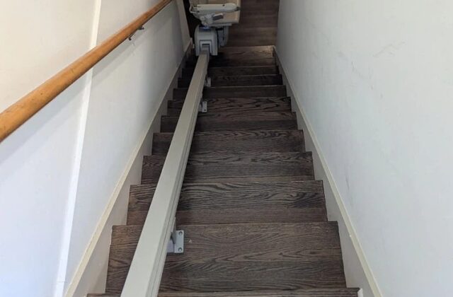 Handicare stairlift rail down dark wooden stairs, chair parked at the bottom