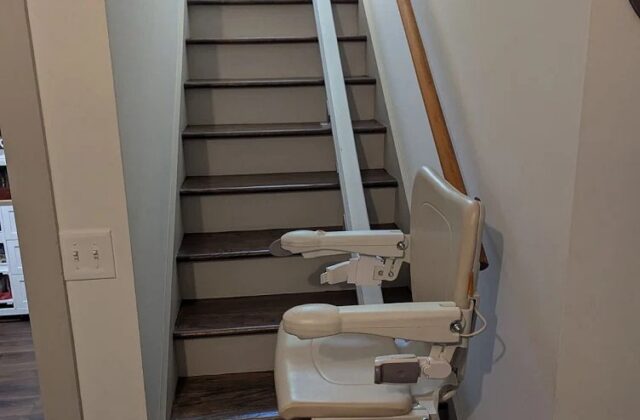 Handicare stairlift on a white rail at the top of stairs with dark treads