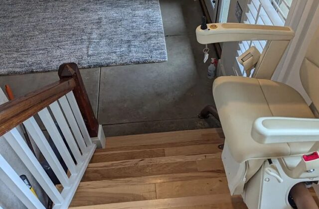 Handicare stairlift parked at the top of light wooden stairs above a living room