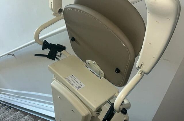 Harmar stairlift folded at the foot of carpeted stairs beside a light switch