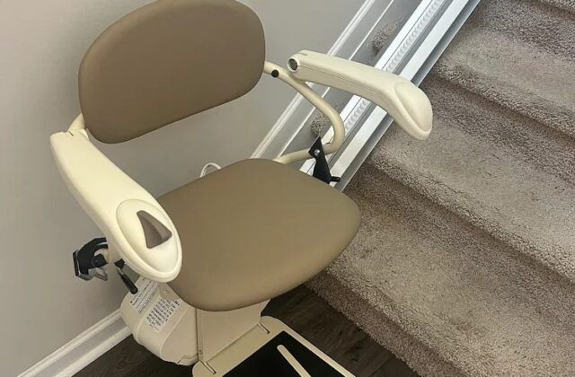 Harmar stairlift with a taupe seat and footrest down at the bottom of carpeted stairs