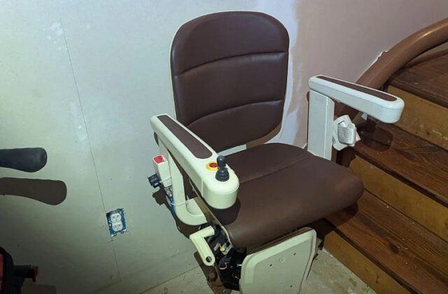 Handicare curved stairlift chair on its rail during a repair, brown seat and armrests