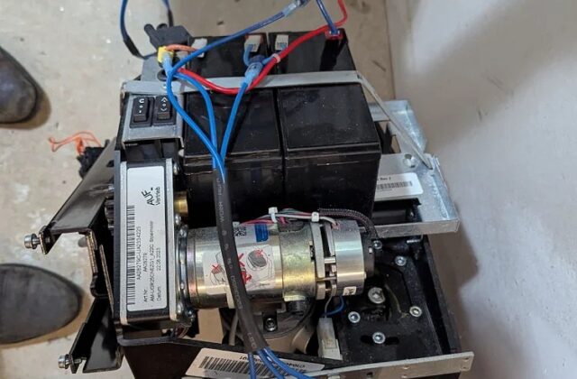 Handicare stairlift drive unit with motor and wiring exposed on a curved rail