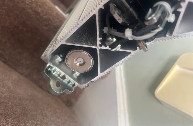 Handicare stairlift rail end with the drive gear and cabling exposed, close up