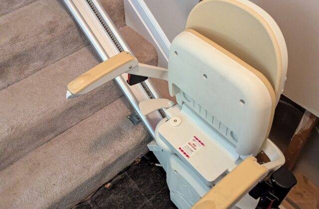 Acorn stairlift with a cream seat at the foot of carpeted stairs on a service visit