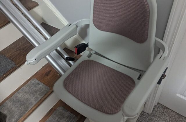 Acorn Superglide stairlift with mauve seat pads at the foot of the stairs on a service visit